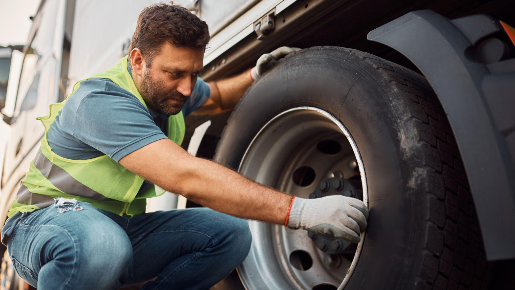 A professional driver conducting a pre-trip tire and wheel inspection on a FreightPoint Peterbilt